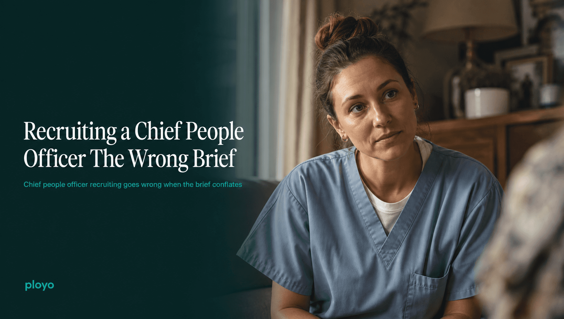 A carer or nurse in soft scrubs, mid-conversation with someone off-frame, listening rather than talking, in a warm domestic interior